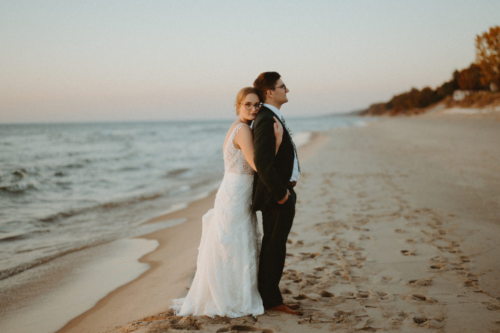 The newly married couple poses on the shoreline of Lake Michigan during sunset for their October wedding.  